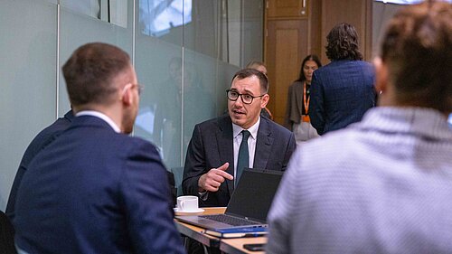 Tom Gordon seated speaking to MPs around a table