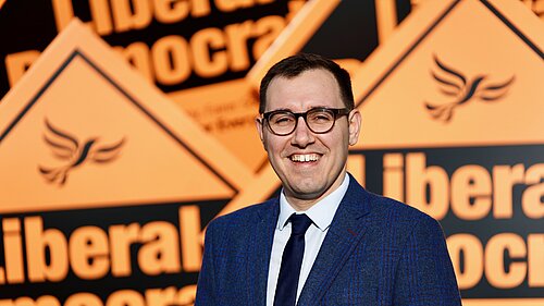 tom stood infront of orange lib dem diamonds