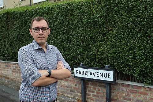 Tom stood infront of a bush with a road sign reading park avenue