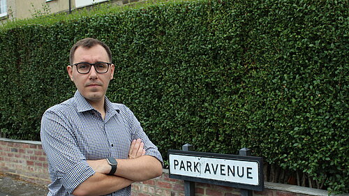 Tom stood infront of a bush with a road sign reading park avenue
