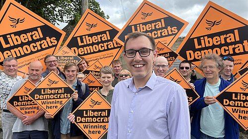Tom Gordon stood in front of supporters holding Diamond shaped placards with Liberal Democrats written on them