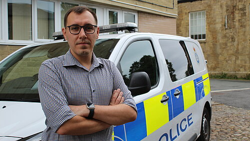 Tom Gordon MP, stood in front of police van.