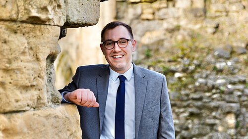 Tom smiling leaning against a wall