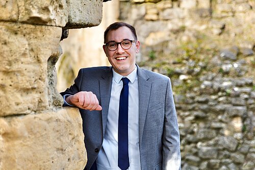 Tom smiling leaning against a wall